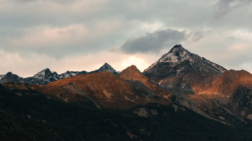 Breathtaking view of mountain peaks adorned with snow under a cloudy sky at dusk.